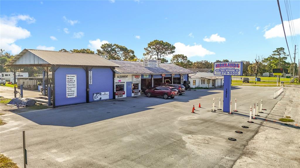 An exterior view of an automotive repair shop with a large parking lot and signage — 16924 SHADY HILLS ROAD, SPRING HILL, FL