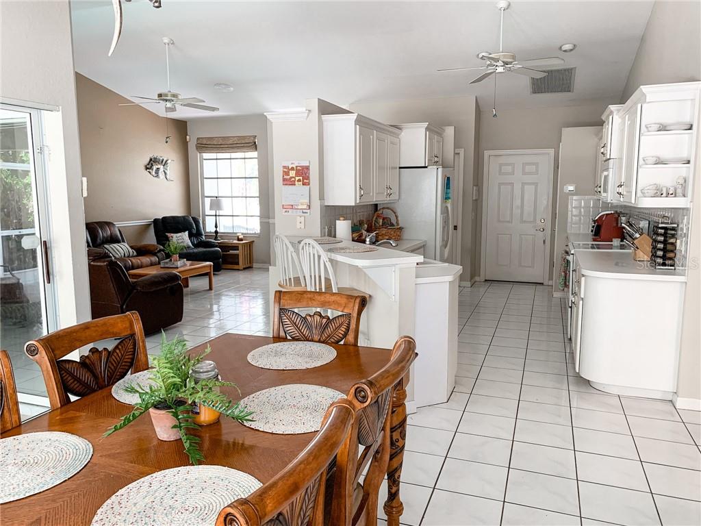 An open-concept kitchen and dining area features white cabinetry, tile flooring, and a wooden table — 1000 CHEVY CHASE STREET, PORT CHARLOTTE, FL