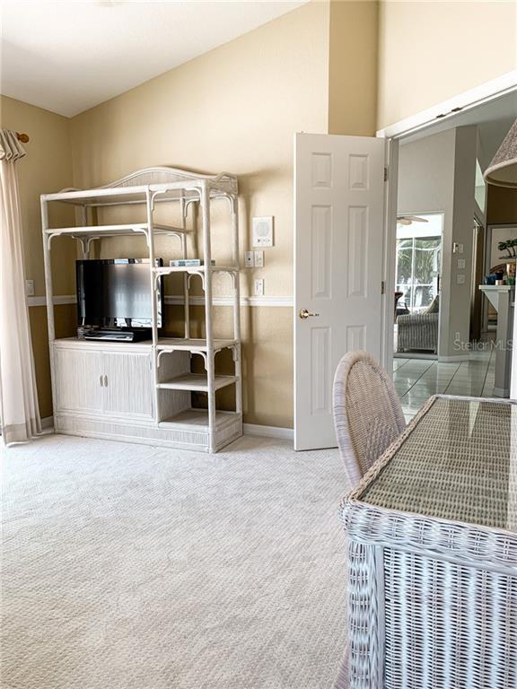 A room features a white wicker entertainment center, carpeted flooring, and a doorway leading outside — 1000 CHEVY CHASE STREET, PORT CHARLOTTE, FL