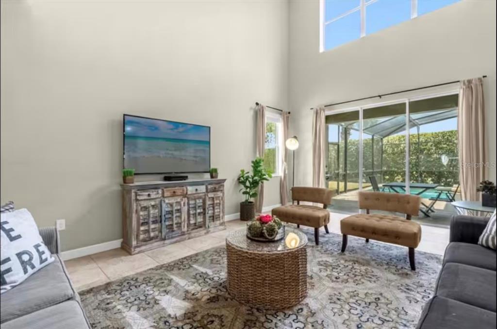 A living room with high ceilings, a television console, two armchairs, and a sliding glass door — 2989 BANANA PALM DRIVE, KISSIMMEE, FL
