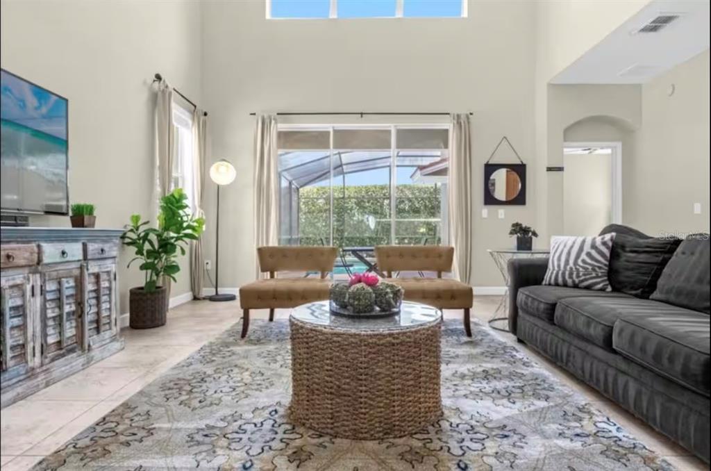 A living room with a dark sofa, two tan chairs, a coffee table, and pool view — 2989 BANANA PALM DRIVE, KISSIMMEE, FL