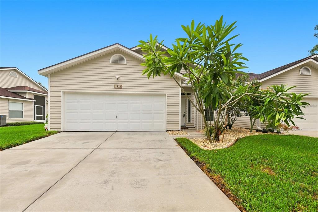 A beige house with a two-car garage and a concrete driveway under a blue sky — 1821 LAKE HERON DRIVE, LUTZ, FL