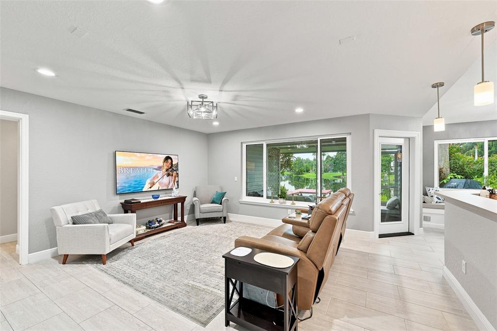 A living room features light gray walls, tile flooring, a leather sofa, and large windows — 1821 LAKE HERON DRIVE, LUTZ, FL