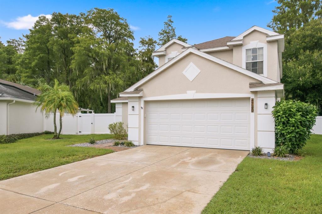A two-story house with a beige stucco exterior, a white garage door, and a concrete driveway — 4730 WOLFRAM LANE, NEW PORT RICHEY, FL