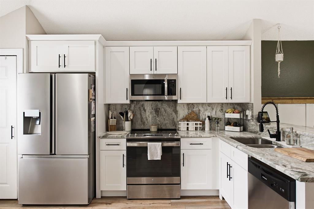 A kitchen features white cabinets, stainless steel appliances, and gray marble-patterned countertops and backsplash — 4730 WOLFRAM LANE, NEW PORT RICHEY, FL