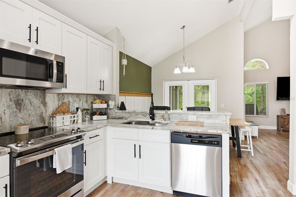 A kitchen with white cabinets, stainless steel appliances, and marble-look countertops overlooks a dining area — 4730 WOLFRAM LANE, NEW PORT RICHEY, FL
