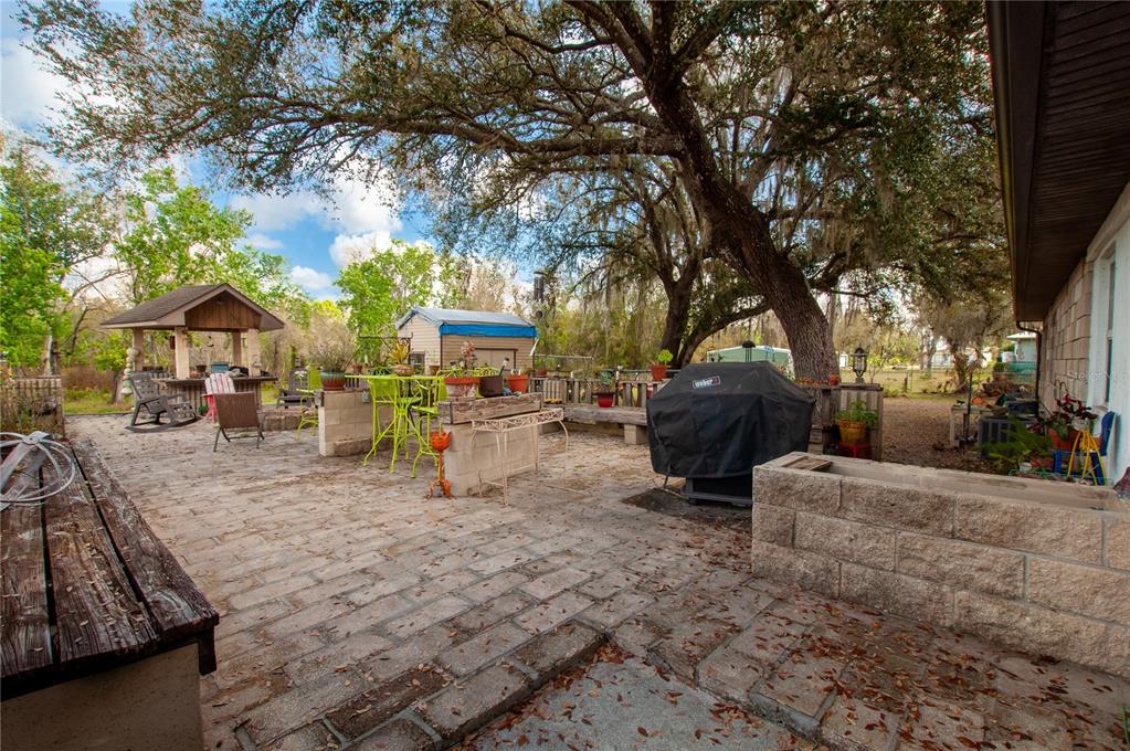 A paved outdoor patio features a covered bar area, a grill, and large oak trees — 2827 SE CREEKWOOD TERRACE, ARCADIA, FL
