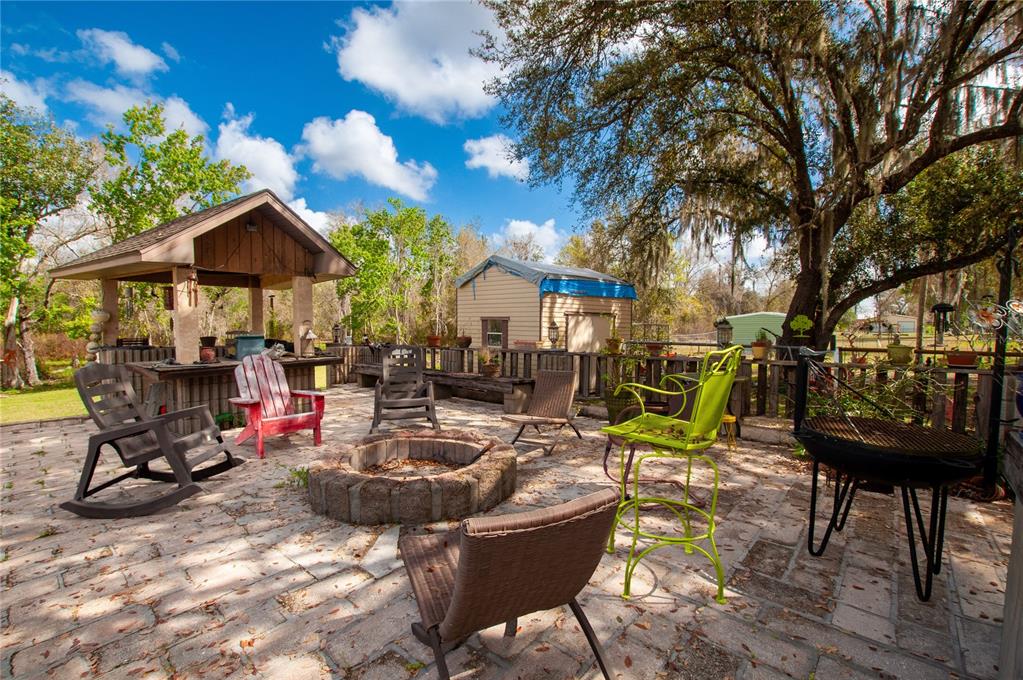 A stone patio features a fire pit, outdoor kitchen, and various chairs under a large tree — 2827 SE CREEKWOOD TERRACE, ARCADIA, FL