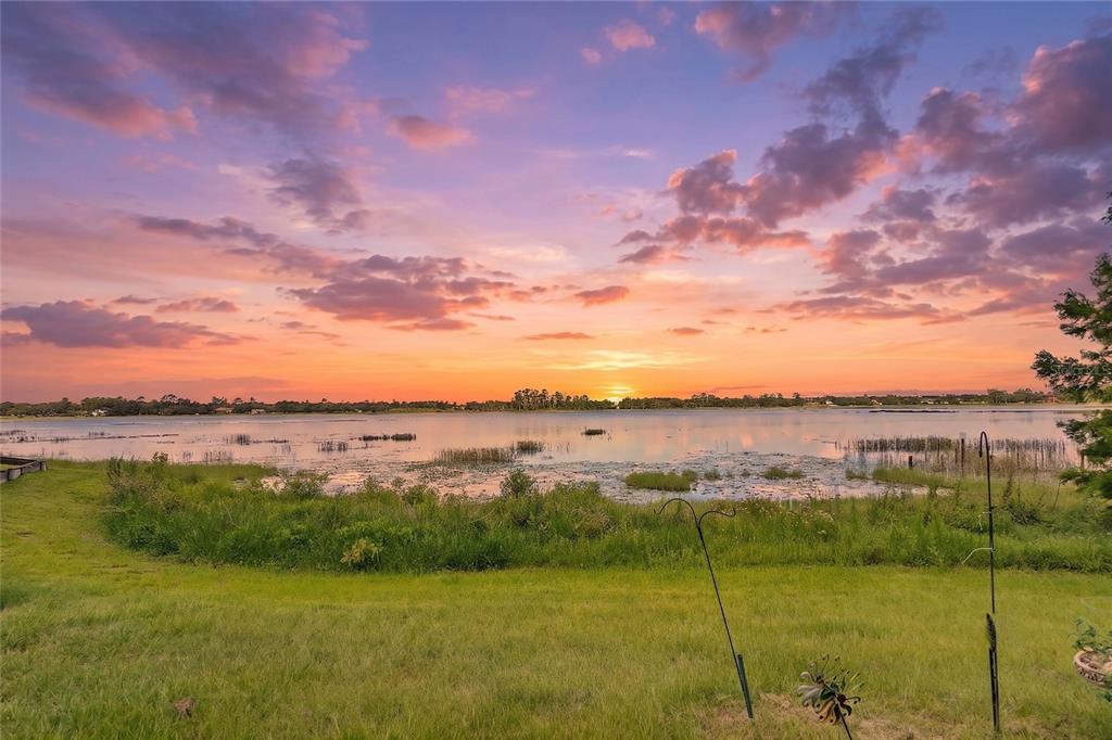 A grassy backyard overlooks a lake during a vibrant sunset with purple and orange clouds — 2372 MITCHELL ISLAND ROAD, DELTONA, FL
