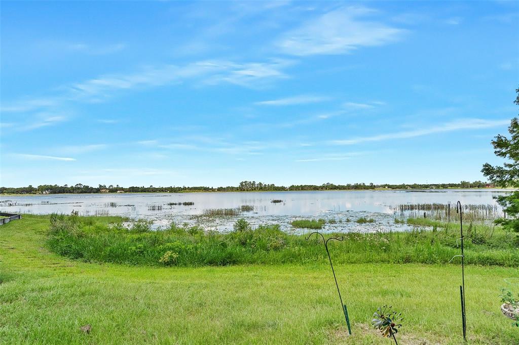 A grassy backyard overlooks a large lake with aquatic vegetation under a blue sky — 2372 MITCHELL ISLAND ROAD, DELTONA, FL