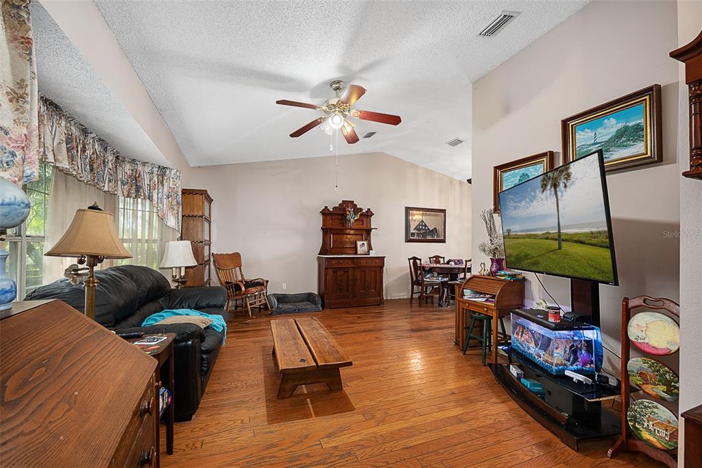 A living room features hardwood floors, a vaulted ceiling with a fan, and a television — 2372 MITCHELL ISLAND ROAD, DELTONA, FL