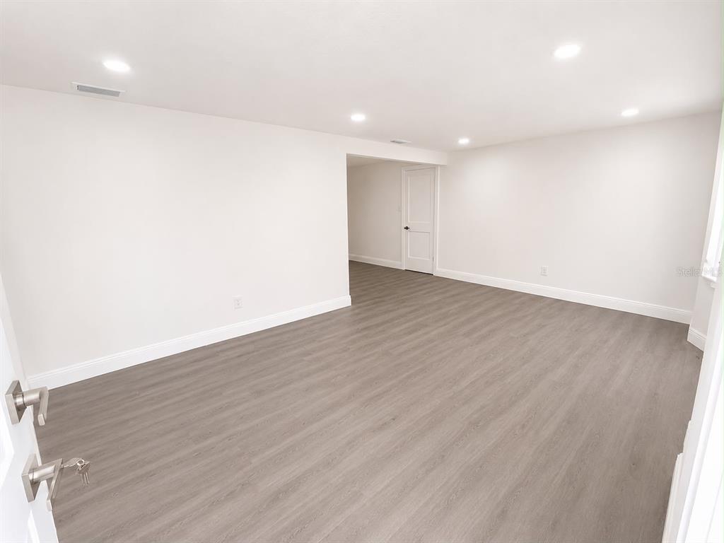 An empty room features light gray wood-look flooring, white walls, and recessed ceiling lighting — 4116 OAKFIELD AVENUE, HOLIDAY, FL