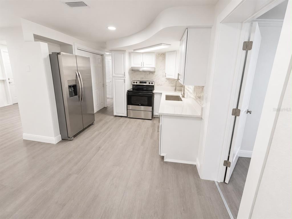 A modern kitchen features white cabinetry, stainless steel appliances, and light wood-look flooring — 4116 OAKFIELD AVENUE, HOLIDAY, FL