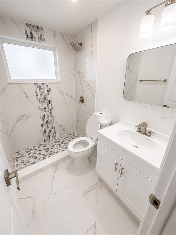 A modern bathroom features a marble-tiled walk-in shower, a white vanity, and a toilet — 4116 OAKFIELD AVENUE, HOLIDAY, FL