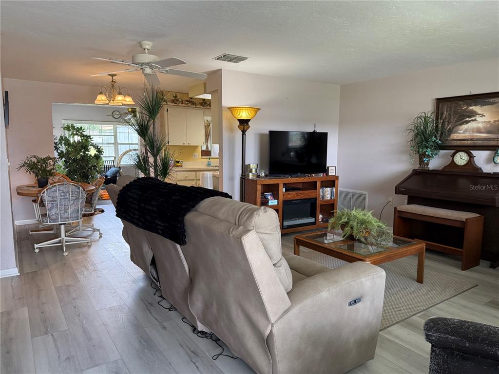 A living room with light wood-look flooring, a beige reclining sofa, and an upright piano — 273 W CASURINA PLACE, BEVERLY HILLS, FL