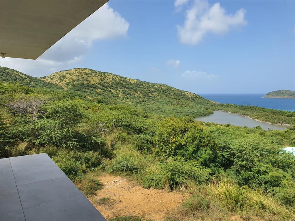 A view from a balcony overlooking a green hillside, a small pond, and the ocean — 8 ALTURAS DE ZONI, CULEBRA, PR