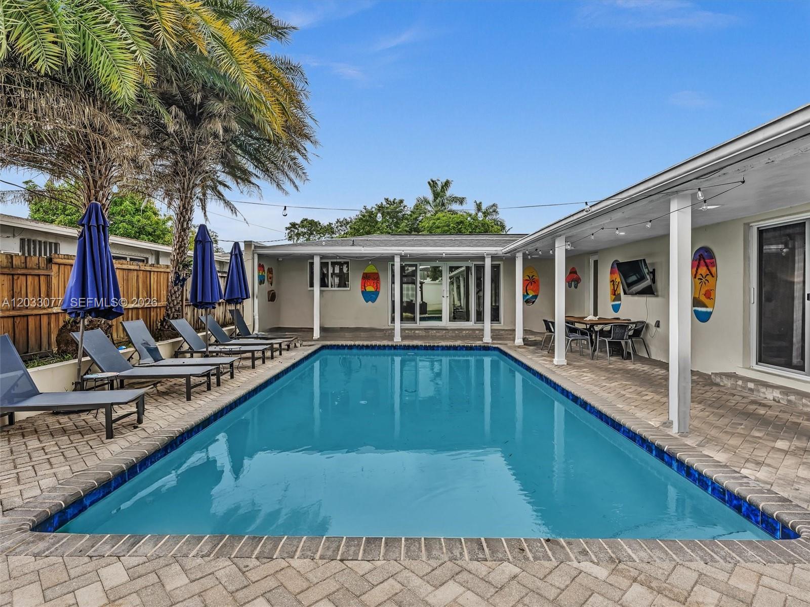 A rectangular swimming pool sits on a paved patio surrounded by lounge chairs and palm trees — 5021 SW 29th Ter, Dania Beach FL 33312, DANIA BEACH, FL