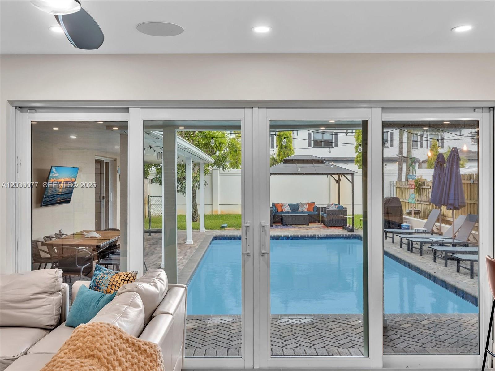 A living room looks out through sliding glass doors onto a patio with a pool — 5021 SW 29th Ter, Dania Beach FL 33312, DANIA BEACH, FL