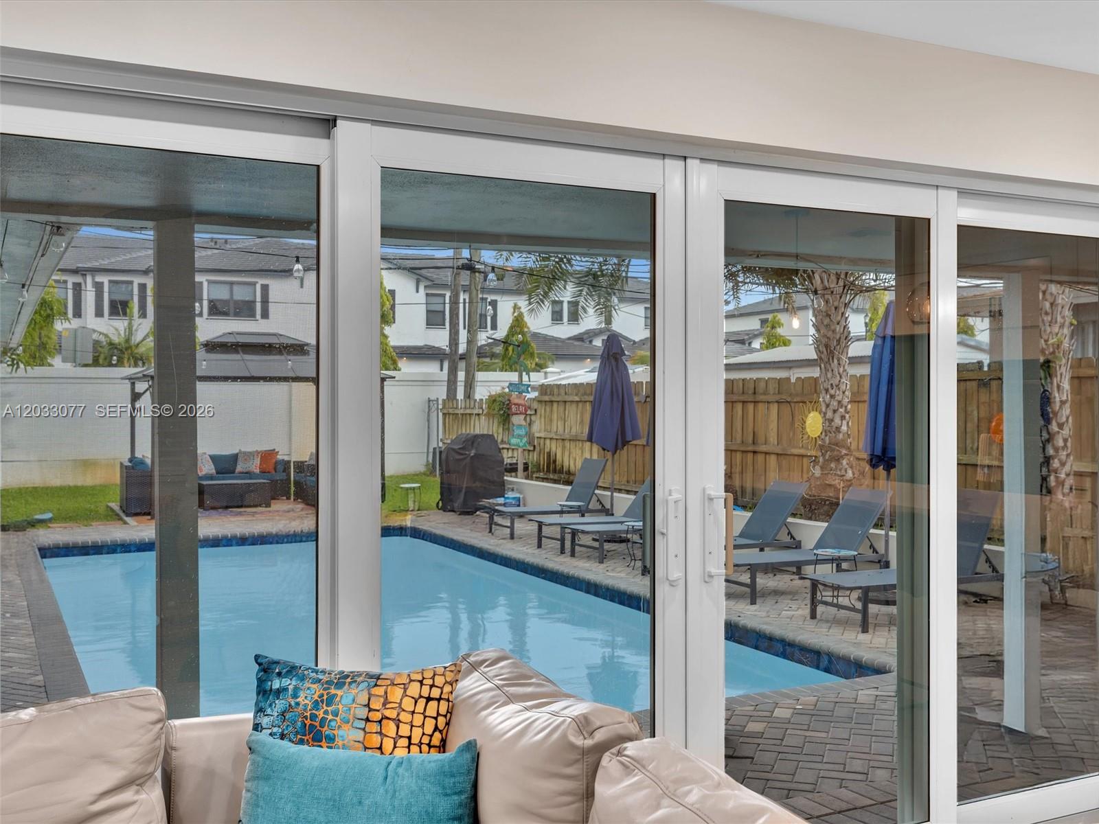 A view through sliding glass doors shows a backyard with a swimming pool and patio — 5021 SW 29th Ter, Dania Beach FL 33312, DANIA BEACH, FL