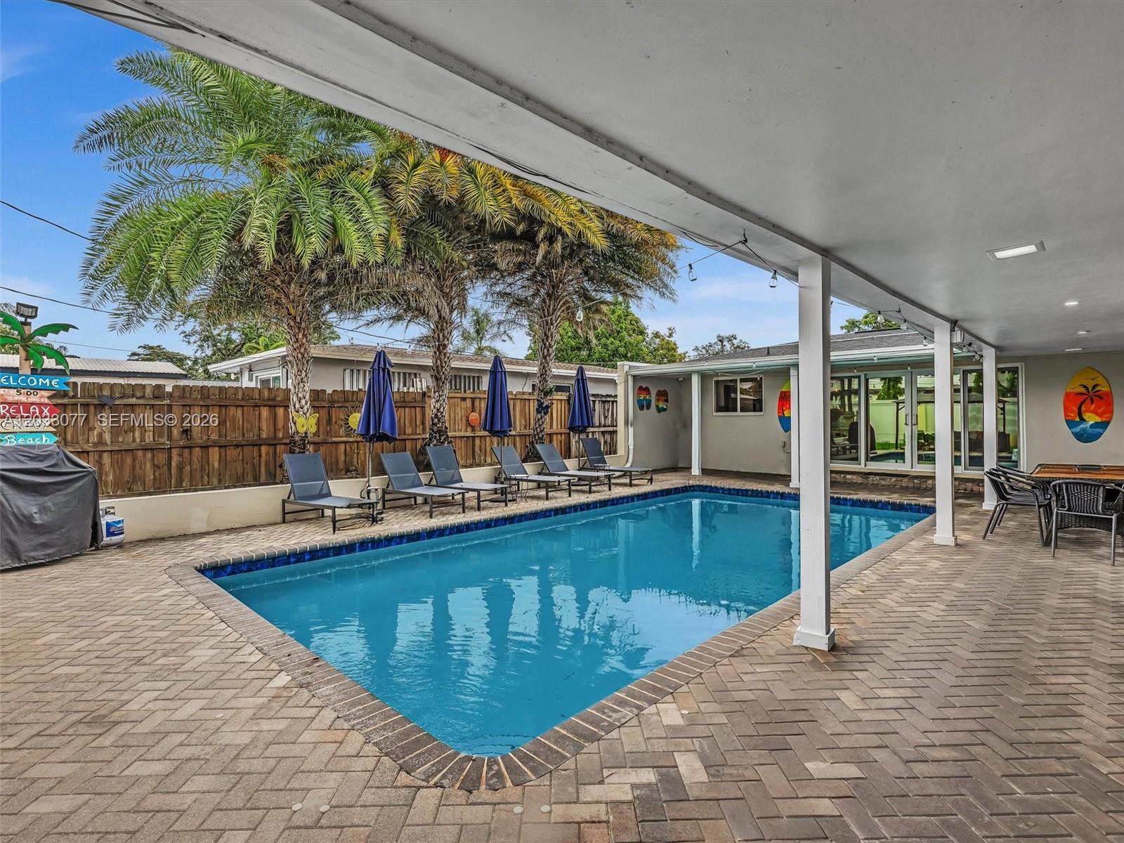 A rectangular swimming pool sits on a brick patio beneath a covered outdoor living area — 5021 SW 29th Ter, Dania Beach FL 33312, DANIA BEACH, FL