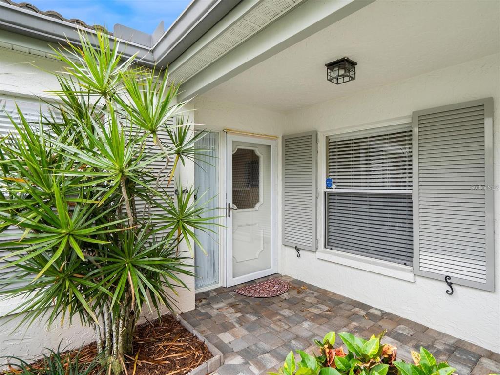 A paved entryway features a white front door, gray shutters, and a large potted plant — 3130 RINGWOOD MEADOW UNIT 44, SARASOTA, FL