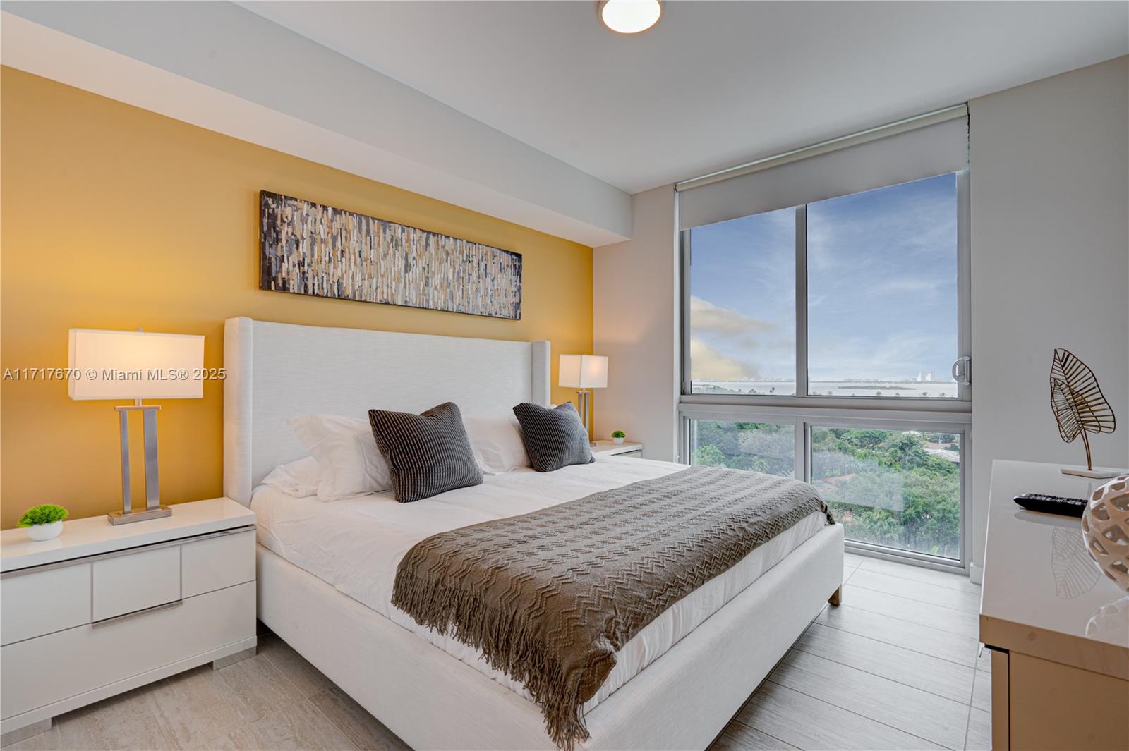 A bedroom features a yellow accent wall, a white bed, and a large window view — 3900 Biscayne Blvd # 717, Miami FL 33137, MIAMI, FL