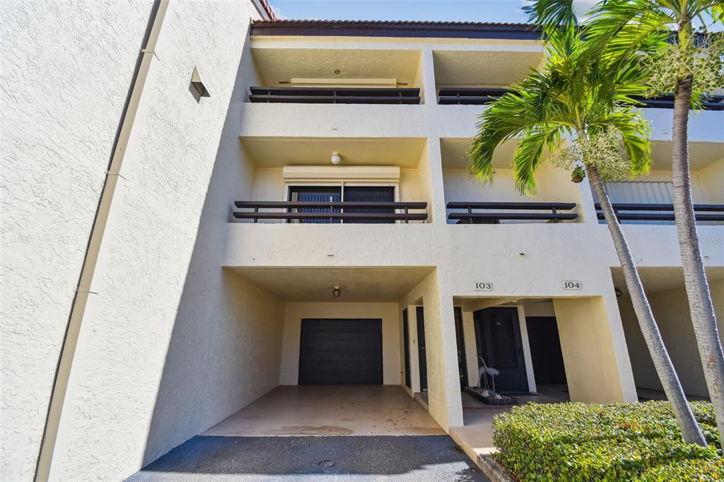 An exterior view of a multi-story building featuring a ground-level garage and unit entrances — 127 1ST STREET E UNIT 103, TIERRA VERDE, FL