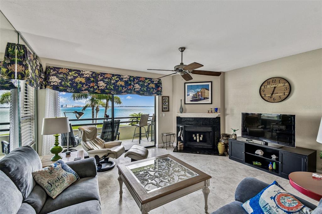 A living room features a fireplace, a ceiling fan, and a balcony overlooking the water — 127 1ST STREET E UNIT 103, TIERRA VERDE, FL