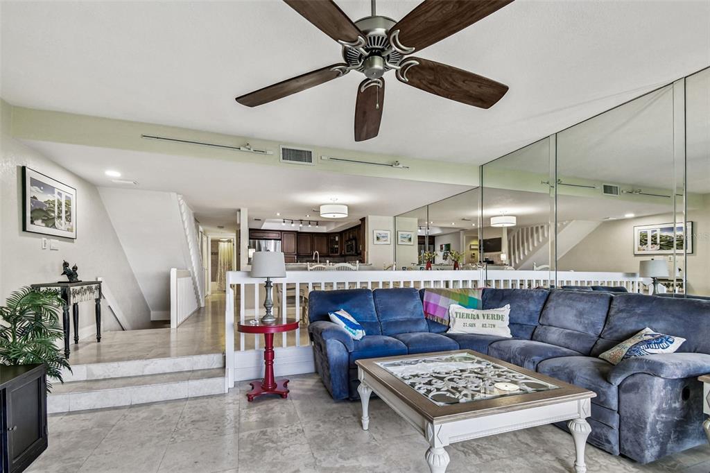 A living room features a blue sectional sofa, a coffee table, and a mirrored wall — 127 1ST STREET E UNIT 103, TIERRA VERDE, FL