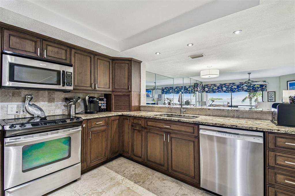 A kitchen features dark wood cabinets, stainless steel appliances, granite countertops, and a tiled floor — 127 1ST STREET E UNIT 103, TIERRA VERDE, FL