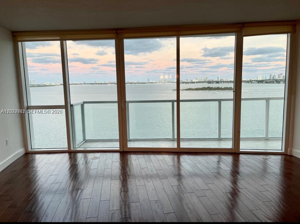 An empty room with dark wood flooring and floor-to-ceiling windows overlooking a bay — 665 NE 25th St # 1102, Miami FL 33137, MIAMI, FL