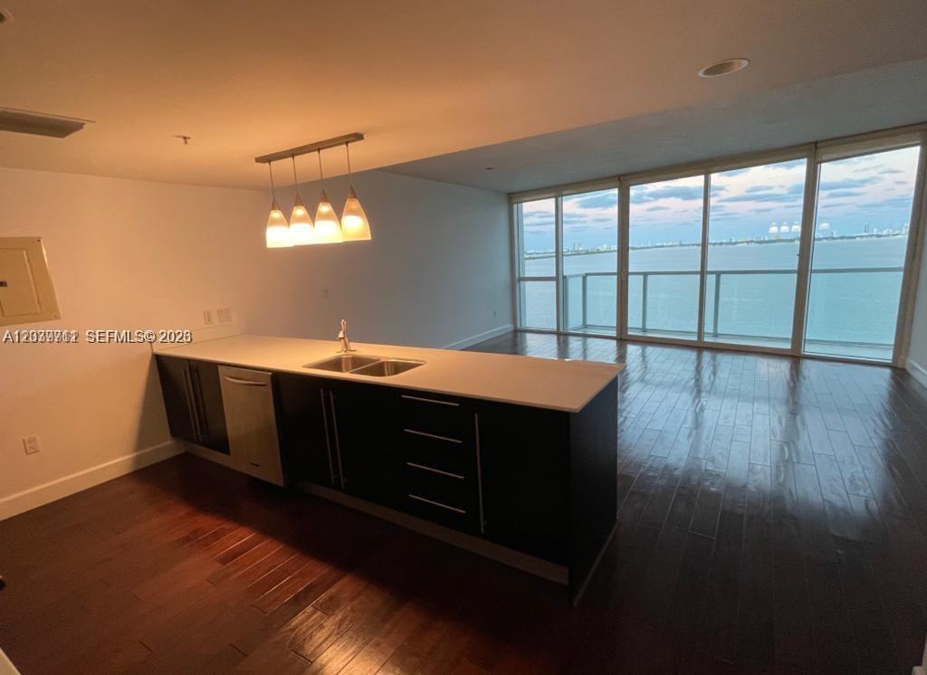 A modern kitchen with dark cabinets and a white countertop overlooks a waterfront balcony — 665 NE 25th St # 1102, Miami FL 33137, MIAMI, FL