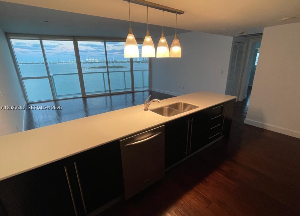 A kitchen island with dark cabinets and a white countertop overlooks a room with water views — 665 NE 25th St # 1102, Miami FL 33137, MIAMI, FL