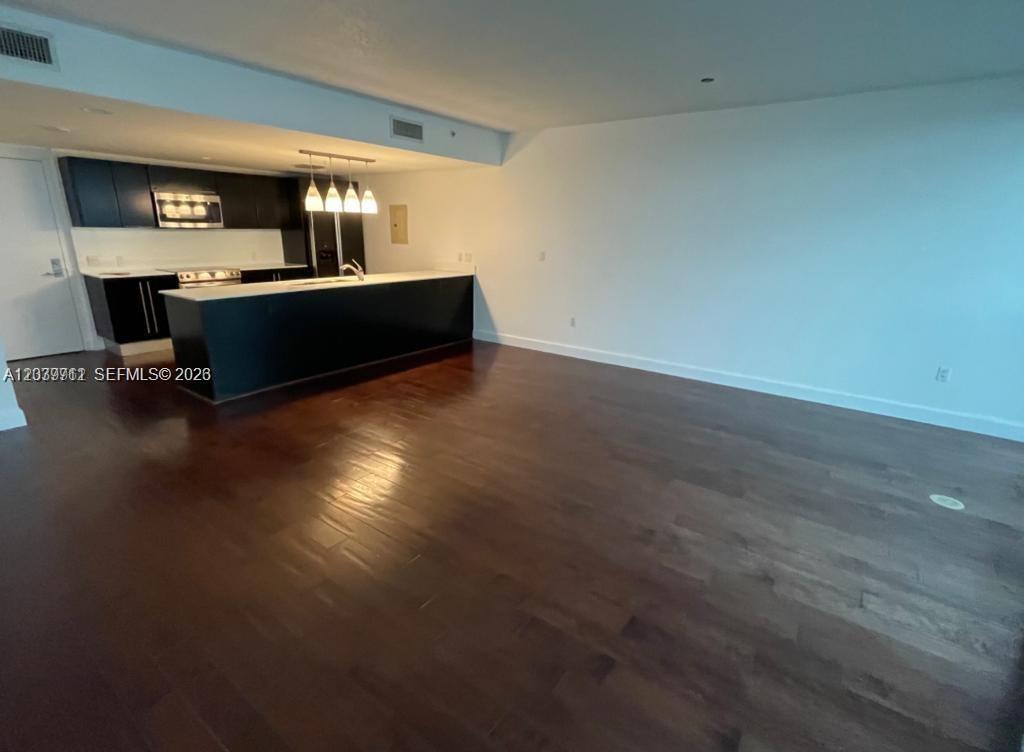 A modern kitchen with dark cabinetry and a large island overlooks an open living area — 665 NE 25th St # 1102, Miami FL 33137, MIAMI, FL