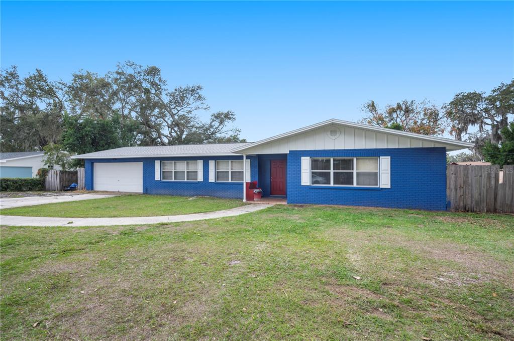 A single-story blue brick house with a white garage door and a red front door — 4911 WHITEOAK DRIVE E, LAKELAND, FL