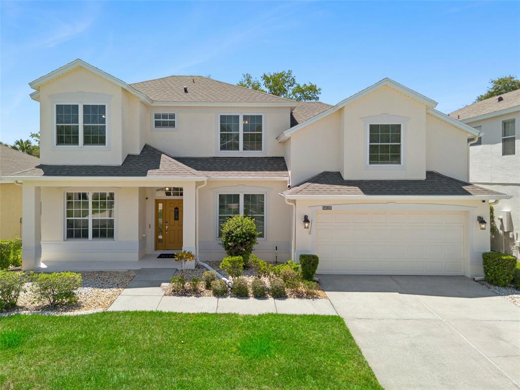 A two-story suburban house with a tan stucco exterior, a front porch, and a garage — 10125 SANDY MARSH LANE, ORLANDO, FL