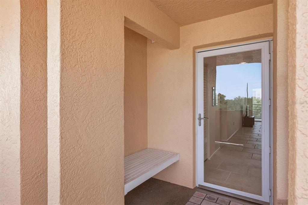 A covered balcony features a built-in bench, textured beige walls, and a glass storm door — 4550 PINEBROOK CIRCLE UNIT 403, BRADENTON, FL