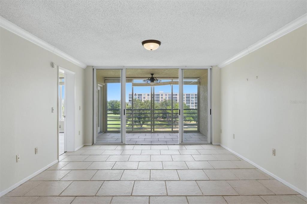 An empty room with light tile flooring leads to a screened balcony overlooking a park — 4550 PINEBROOK CIRCLE UNIT 403, BRADENTON, FL