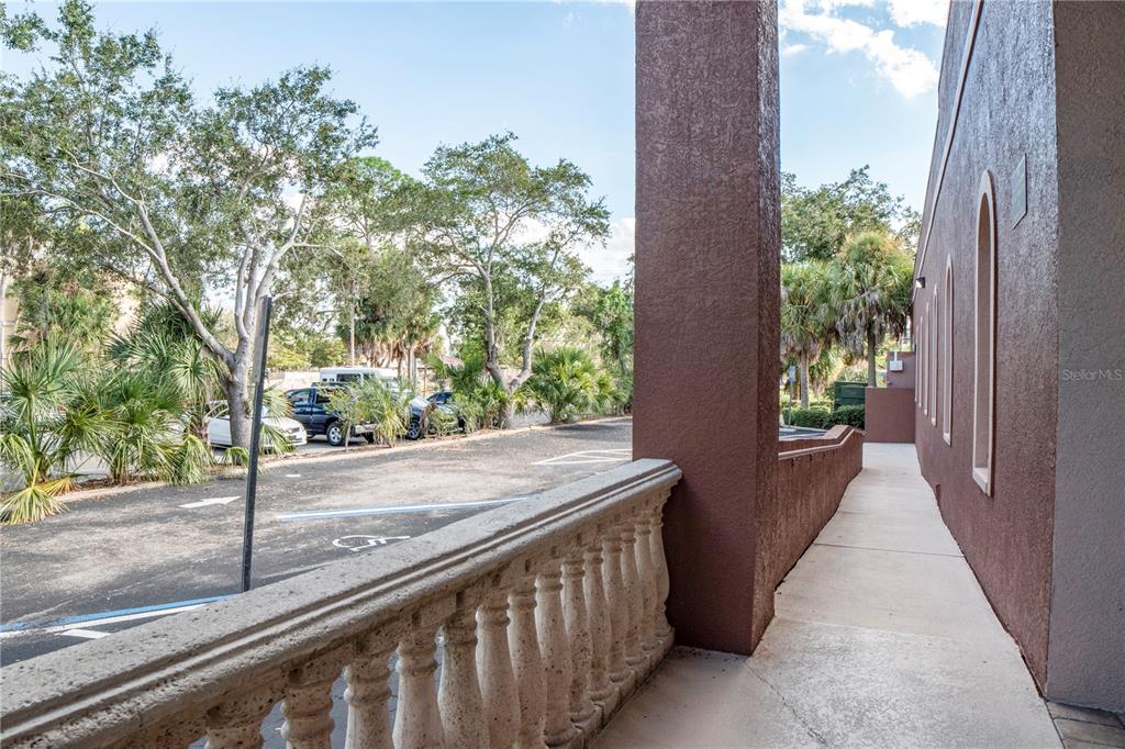 A concrete walkway with a stone balustrade runs alongside a brown stucco building exterior — 2484 CARING WAY UNIT F, PORT CHARLOTTE, FL