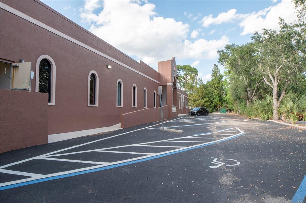 A brown building exterior features arched windows and a paved parking lot with handicap markings — 2484 CARING WAY UNIT F, PORT CHARLOTTE, FL