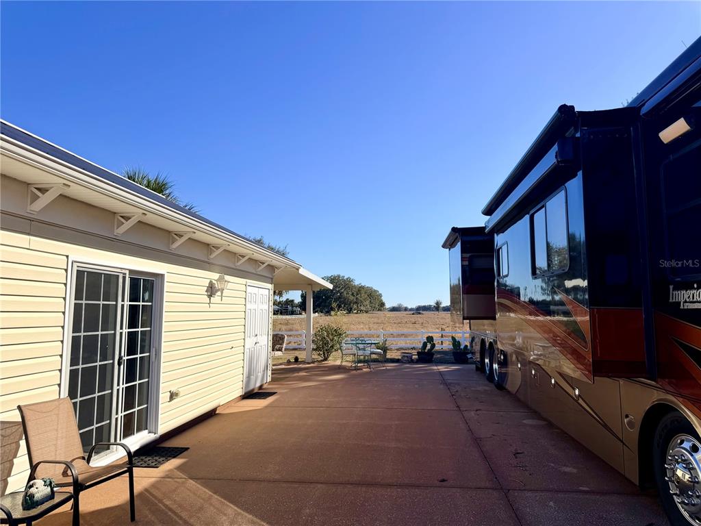 A paved patio area sits between a house with sliding glass doors and a large RV — 4805 SE 94TH AVENUE, WEBSTER, FL