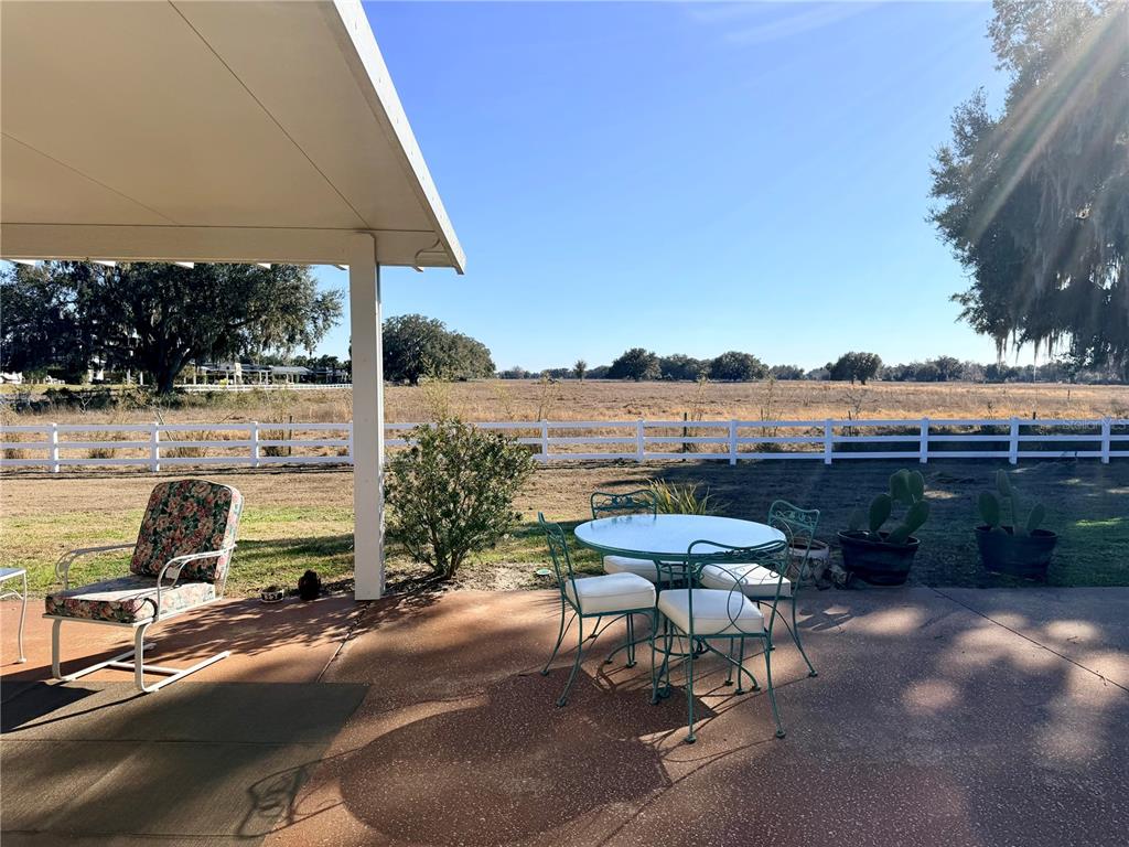 A covered patio features a floral chair, a metal dining set, and a white fence — 4805 SE 94TH AVENUE, WEBSTER, FL