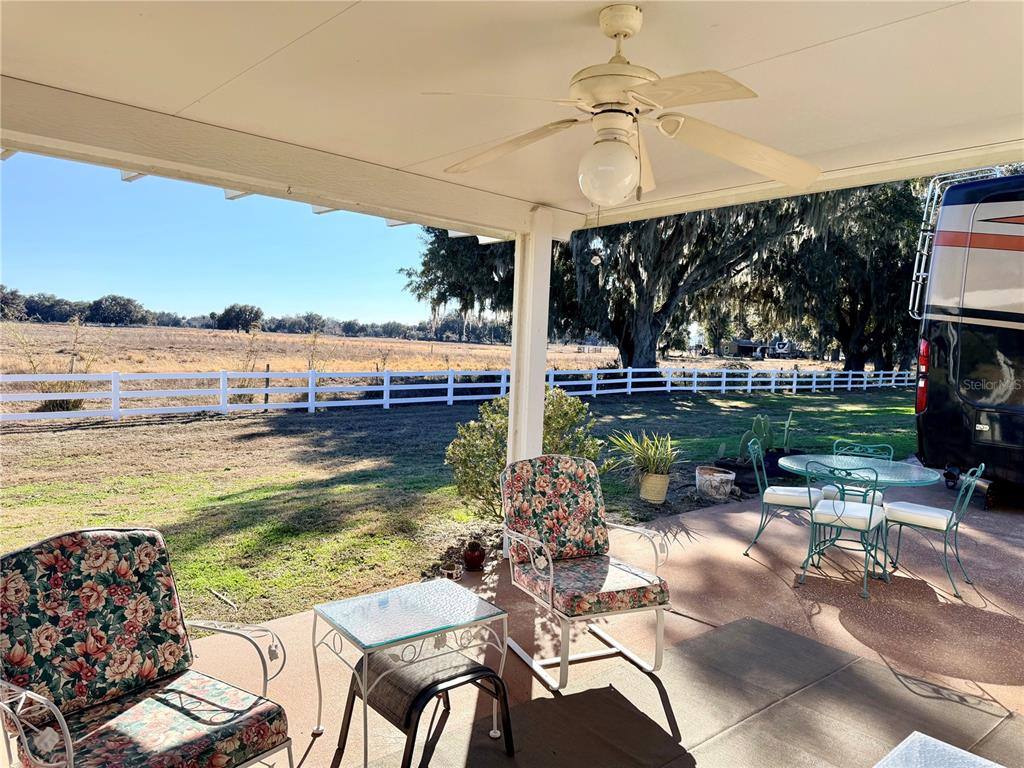 A covered patio features floral-cushioned chairs, a glass-top table, and a view of a fenced field — 4805 SE 94TH AVENUE, WEBSTER, FL