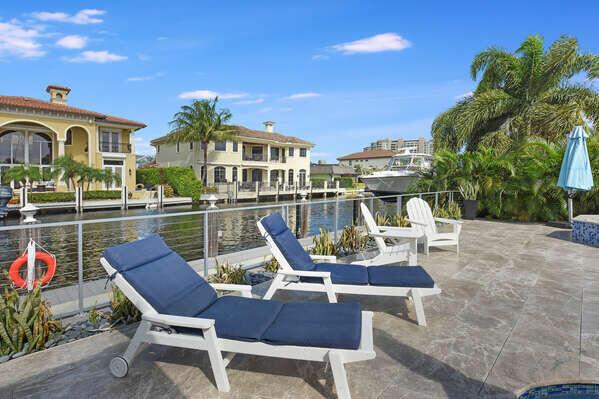 A patio with lounge chairs overlooks a canal with houses and a boat in the background — 839 Enfield Street, Boca Raton FL 33487, BOCA RATON, FL