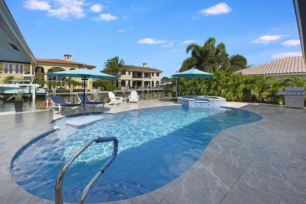 A swimming pool and hot tub on a stone patio overlooking a canal and houses — 839 Enfield Street, Boca Raton FL 33487, BOCA RATON, FL