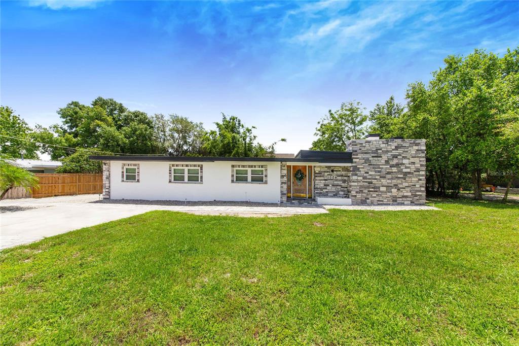 A single-story house features a white exterior, stone chimney, and a flat roof — 1004 AVENUE G NE, WINTER HAVEN, FL