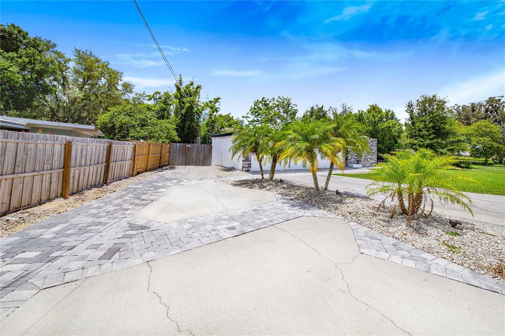 A paved driveway leads to a white building with palm trees and a wooden fence — 1004 AVENUE G NE, WINTER HAVEN, FL
