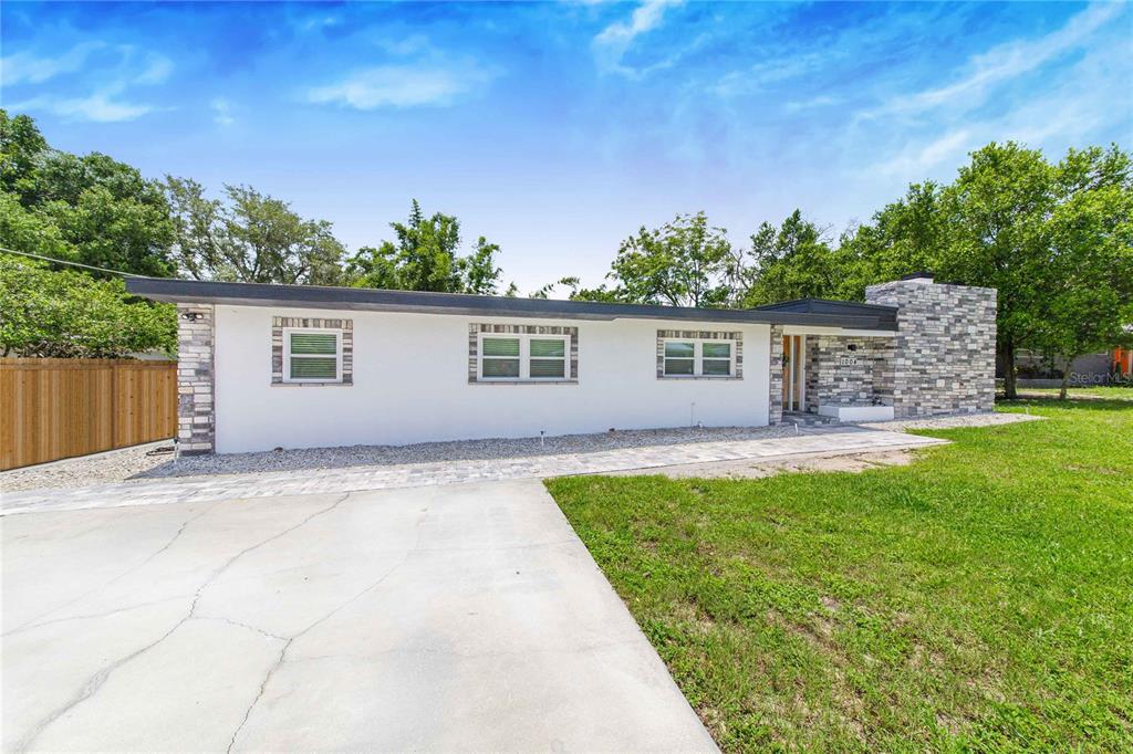 A single-story house with a white exterior, stone chimney, and a paved driveway — 1004 AVENUE G NE, WINTER HAVEN, FL