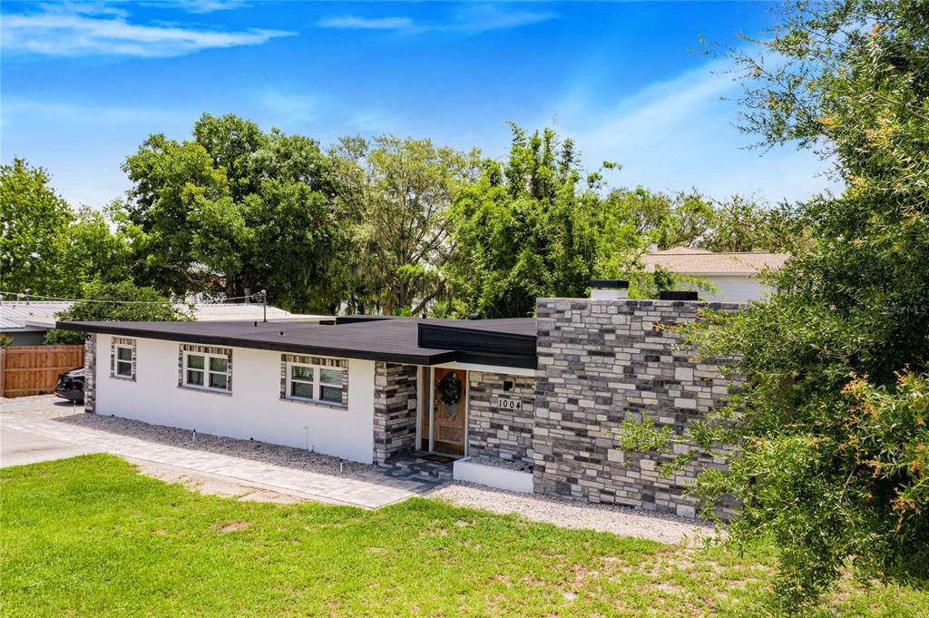 A single-story house with a flat roof, white walls, and a stone-clad chimney facade — 1004 AVENUE G NE, WINTER HAVEN, FL