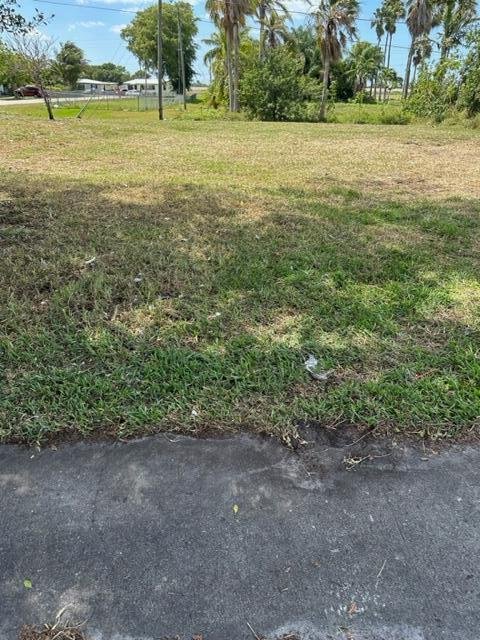 A grassy, vacant lot is viewed from the edge of an adjacent paved road — 501 W Baines Terrace, Pahokee FL 33476, PAHOKEE, FL